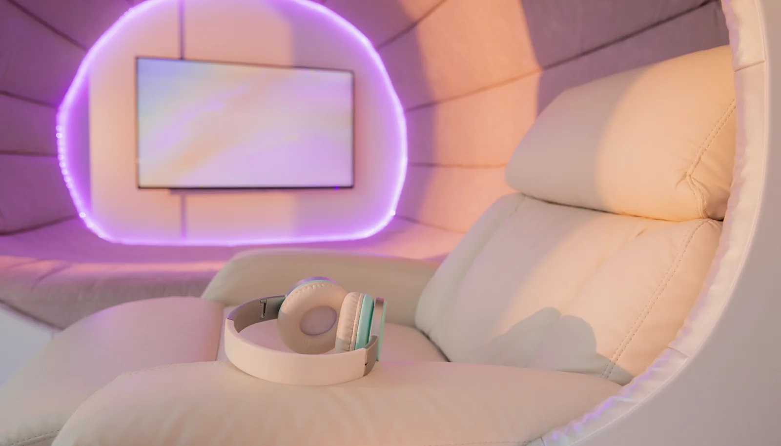 Inside a La Vida Rose soundproof pod — a plush cream recliner with premium headphones, a wall-mounted screen and soft lilac LED lighting